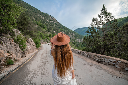 穿着棕帽子和白衣服的女性旅行者 看着令人惊叹的山峰和森林 漫游概念 大气史诗时刻假期树木旅行爬坡自由远足流浪者荒野女孩背包图片