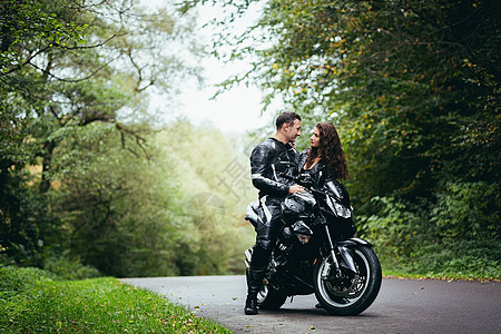 英俊的年轻男子和美丽的年轻女孩 一对夫妇坐在摩托车上 站在一辆穿着黑色皮衣的摩托车旁边 在大自然中拥抱 在街上男人女朋友女性幸福图片