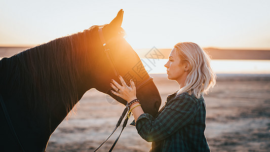 金发女郎骑着拥抱马 美丽的黑种马女士享受日落的自然 爱与友谊的概念 笑声摄影蓝色鬃毛天空跑步马术场地力量农场家畜图片