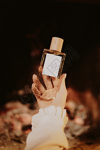 女性手中的精美微薄香水瓶子有壁炉火焰背景 芳香和本质概念图片