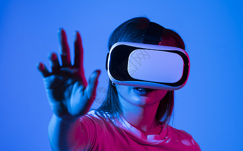 穿着白色T恤的激动人心的黑发女人 利用VR头套眼镜 体验到虚拟现实的光辉闪耀着银色的手娱乐女孩女士技术视频微笑耳机空气模拟器电子图片