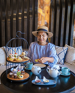 亚裔妇女在豪华豪华高端茶 在豪华酒店吃零食喝茶小吃蛋糕糕点杯子长笛咖啡英语女性帽子餐厅图片