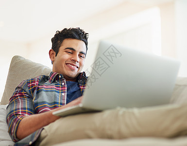 一位英俊的年轻人使用笔记本电脑在家沙发上休息时使用笔记本电脑图片