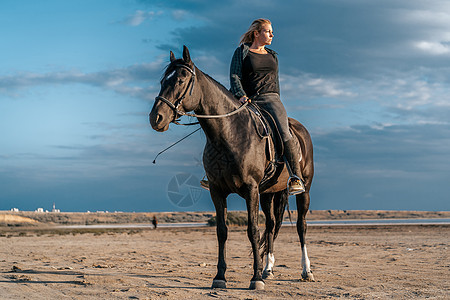 女人骑着马在美丽的秋季自然景观上通过河流或湖泊 太阳耀斑 美丽的背景 农场动物 训练 赛马的概念牧场自然哺乳动物行动场地自由马术图片