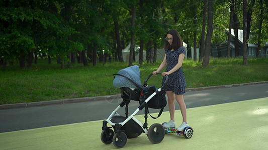 一名年轻女子推着婴儿车在气垫板上行走 一位现代母亲带着孩子散步 戴眼镜和裙子的女孩图片