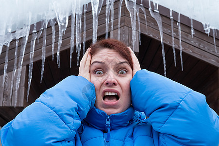 一个惊恐的女人站在一个有大冰棒的屋顶下 冬天很危险门廊冰柱外套季节事故冒险温度女性眼镜天气图片