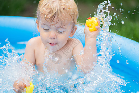 可爱的小孩在院子里的蓝色街池里和鸭子一起洗澡 快乐的蹒跚学步的孩子 宝贝的画像 孩子笑 泼水 微笑 健康生活方式 家庭 夏季休闲图片