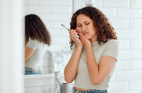 牙痛 疼痛和敏感的牙齿 一个女人在家里的浴室里刷牙 有蛀牙的年轻女性在日常口腔卫生过程中感到不适 嘴巴疼的女士图片