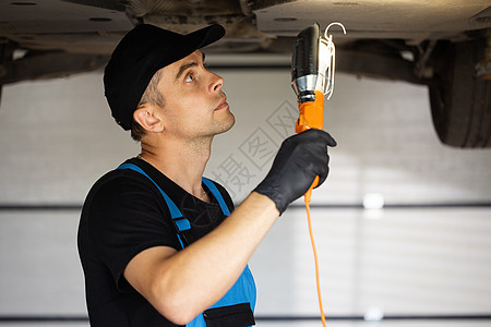 在车间工作的带灯的蓝色工作服的汽车机械师 专业机械师正在汽车服务中修理汽车 汽车服务 维修 保养和人的概念图片