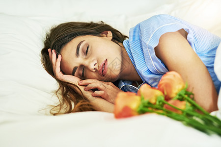 一位迷人的年轻女人睡在床上的鲜花旁睡觉 她是个有魅力的年轻女子图片