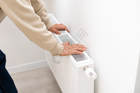 一位老人用电暖器暖手 淡季 集中供暖延迟 尽管电费增加 但人们不得不购买额外的加热器以保持房屋温暖图片