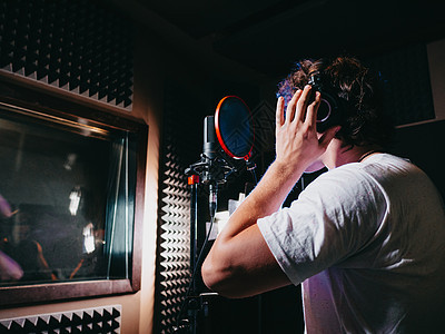 年轻英俊的歌手在演播室戴上耳机 录制新的旋律或专辑 男性声乐艺术家 有卷发准备工作广播安慰编辑女性嗓音记录星星音乐播送打碟机图片