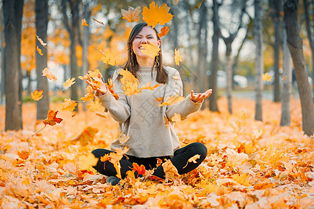 快乐的秋天年轻女人微笑着快乐地在秋天的森林里吐出秋天的落叶 混血白种人 中亚女人图片