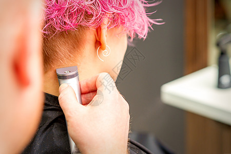 后面看美容师的手剃胡须和颈部 与电动短片 年轻caucasian女人 在美容院 短粉色头发理发师发型师剪发理发店发型沙龙服务造型图片