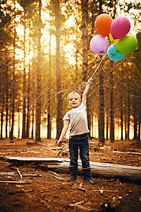 气球让我兴奋 一个快乐的小男孩拿着一束气球站在外面的树林里图片