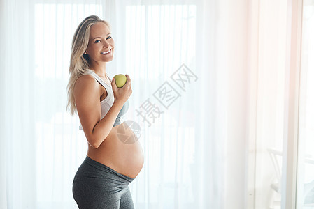 我的宝贝喜欢我吃好东西的时候 穿着运动服在家里吃苹果的快乐孕妇的肖像 (笑声)图片