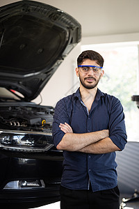 肖像短胡子英俊的汽车机械师正在驾车服务中工作 他身穿让式衬衫和安全眼镜 双臂交叉 专家经理看镜头图片