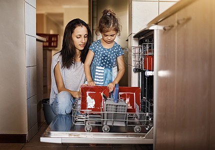 抚养一个负责任的小女孩 一个可爱的小女孩和她妈妈一起在家里装洗碗机图片