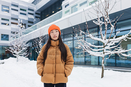 在冬天寒雪天走在街上 穿着温暖的亚洲女孩 穿着夹克和橙色热帽的女人肖像微笑太阳成人化妆品天气木头享受女性降雪季节图片