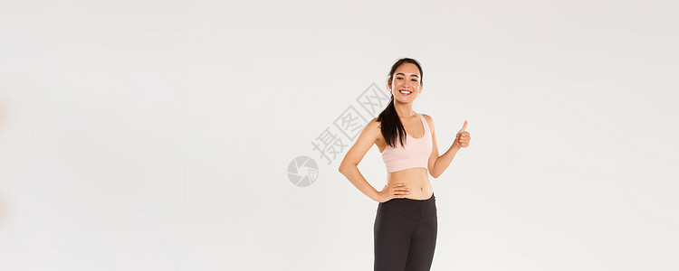 全长满意的微笑 可爱的亚洲健身女孩 穿着运动服的女运动员竖起大拇指 微笑着高兴 骄傲的女运动员获得每日锻炼目标 白色背景身体情绪图片