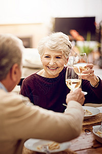 一对年长的夫妇 喝着葡萄酒杯烤面包 而他们在家里享受一顿饭图片