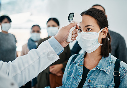 一位戴着口罩的女游客在机场等候登机时用红外线温度计测量体温 冠状病毒大流行期间的旅行限制图片