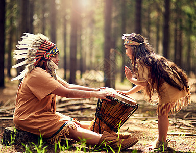 一个小女孩在树林里 和母亲一起装扮时 敲着一个鼓 然后和她妈妈玩耍图片