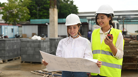 两名身着安全头盔和黄色背心的建筑女建筑师 检查工业建筑建筑工地图片