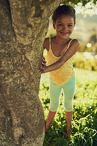 这里没人会找到我 一个微笑的女孩在树后面玩耍的肖像图片