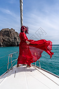 夏日在游艇上穿着红色礼服的中年女子 有吸引力的中年妇女 豪华暑假冒险 户外活动帆船女性娱乐运输幸福方向盘血管双体微笑海滩图片
