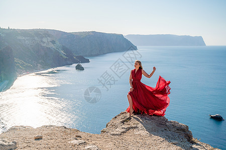 一个穿着红色飞行服的女人 在大海的背景下 飘在风中发抖着自由太阳成人丝绸海洋幸福魅力女孩飞行尾巴图片