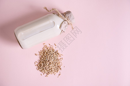 粉红色表面上有一堆燕麦片和一瓶植物性有机健康燕麦奶 素食有益健康的不含乳制品的饮料图片