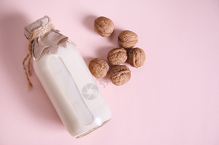 以粉红色背景和复制空间为原料 配有有益植物的牛奶和胡桃以及香味食品和饮料的瓶装瓶图片