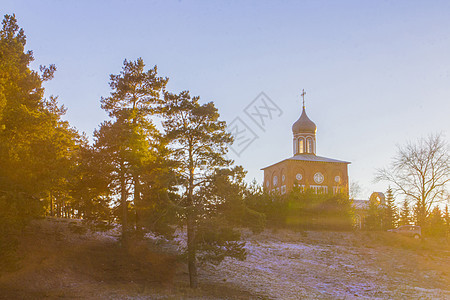 森林附近山丘上的东正教教堂 冬季日落风景图片