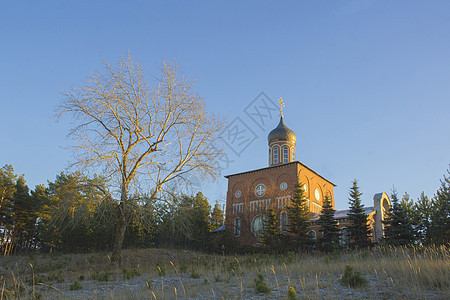 森林附近的一座山丘上的东正教教堂 秋季日落风景图片