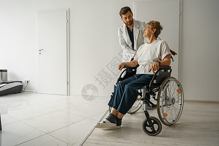 专业男医生 在医疗诊所大厅内用轮轮椅接送女病人男性老年医院援助车轮护理保健治疗师专家欢呼图片