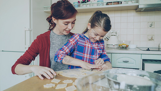 快乐的妈妈和可爱的小女儿坐在家里的现代厨房里 用面包店的形式一起聊天和做饼干 家庭 食物和人的概念图片