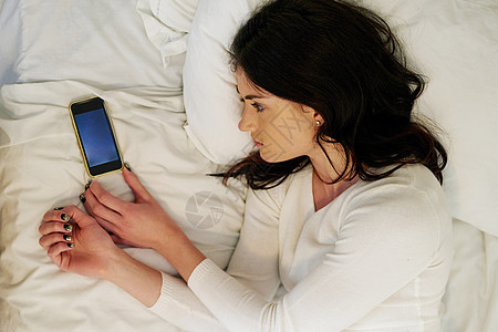 她还在等他的电话 一位年轻女人躺在床上 看着她身边的手机 (笑声)图片
