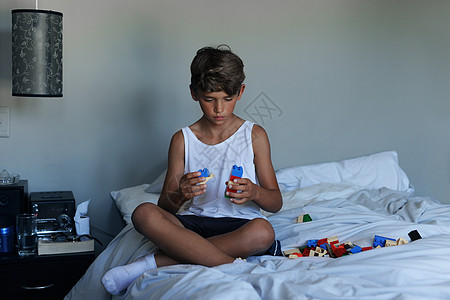 儿童游戏一个在家里床上玩玩具的年轻男孩 以他的想象力为依托背景