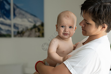 母亲和孩子在一张白色的床上 穿着尿布的妈妈和男婴在卧室里玩耍 父母和小孩在家里放松 一家人在一起玩得很开心婴儿童年房间男生玩具儿图片