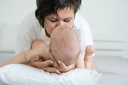 母亲和孩子在一张白色的床上 穿着尿布的妈妈和男婴在卧室里玩耍 父母和小孩在家里放松 一家人在一起玩得很开心拥抱毯子睡眠女孩母性房图片