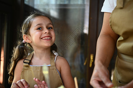 可爱的漂亮孩子 小姑娘穿着美食厨师围裙 微笑着快乐的牙色笑容和妈妈一起做饭图片