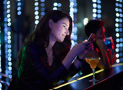 你什么时候到俱乐部 一位面带微笑的年轻女子坐在一家夜总会的吧台旁阅读短信图片