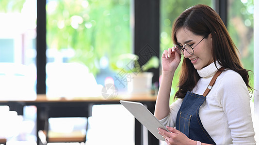 站在咖啡馆时使用数码平板电脑微笑着围裙的企业家图片
