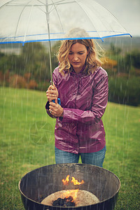 继续燃烧火焰 一个女人在雨中烧烤 同时拿着伞看着火焰 (掌声 贾宝玉)图片