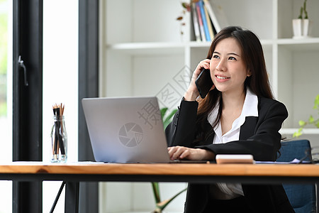 深思熟虑的女商务人士在移动电话上讲话 并使用电脑笔记本电脑图片