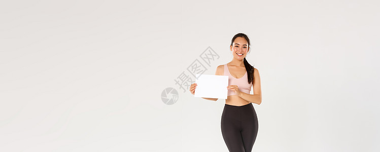 全长微笑漂亮的亚洲黑发女运动员 穿着运动服的女运动员在空白纸上展示标志 广告健身房会员或健身器材特价训练情绪举牌子身体成人肌肉女图片