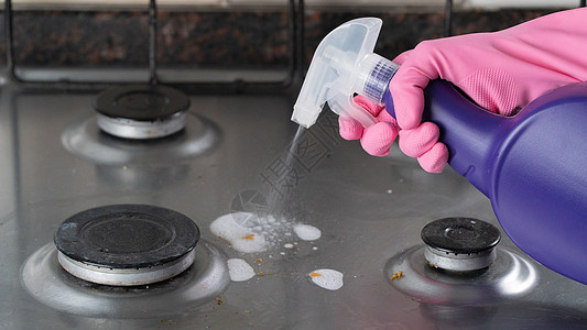 一只手握在粉色手套上喷洒洗涤剂 放在肮脏的清洁用煤气炉子上图片