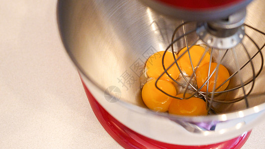 生鸡蛋放在一个金属碗的永久性搅拌机里 在厨房搅拌机里准备配糖的蛋黄蛋糕面团美食面包桌子框架奶油鞭子食物混合器图片