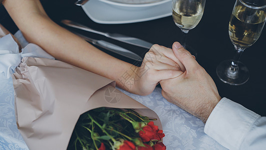 男性手拿着香槟杯和鲜花在桌子上握住和挤压女性手的特写镜头 浪漫关系 爱情和美食概念图片